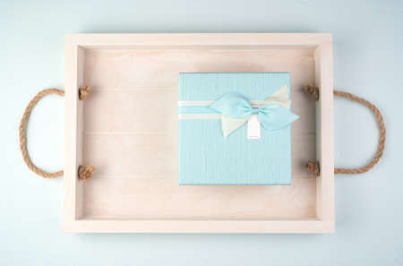 Soft blue gift box with a bow on a white tray. The view from the top. Concept of holidays and gifts.
