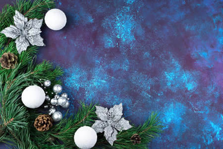 Green pine branches are decorated with beautiful silver flowers, cones and Christmas toys on a blue...