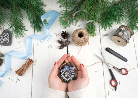 Wooden Christmas tree in the hands of a woman on a background of blue ribbon, threads, fir branches. Holiday background, top view. The concept of the new year 2021, Christmas.の写真素材