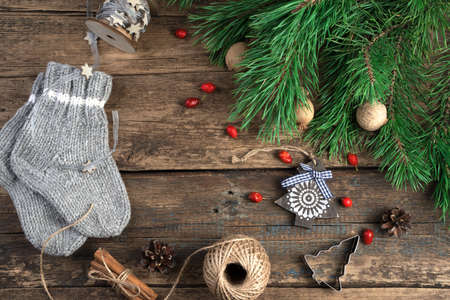 Cozy, cute Christmas background with fir branches, wooden Christmas tree, childrens knitted socks, rose hips, cinnamon and ribbon on a natural wooden background. The concept of New year and Christmasの写真素材