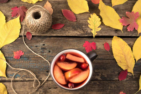 Mug with hot tea with fruit and rose hips on a natural wooden background with autumn leaves. Top view with space to copy. The concept of thanksgiving or Halloween.の写真素材