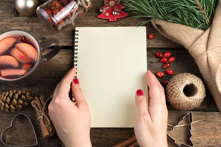 A womans hands open a notebook against a background of pine branches, cups of mulled wine, cinnamon and berries on a wooden background. Cozy composition. The concept of New year and Christmas.の写真素材