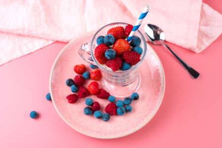 Creamy cocktail with raspberries, strawberries and cereals on a soft pink background. Concept of...