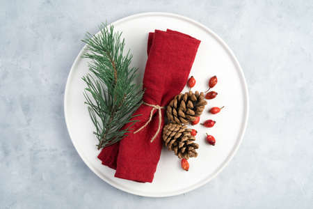 Christmas table setting, white plate decorated with napkin and pine branches and fir branches. Holiday background, top view.の写真素材