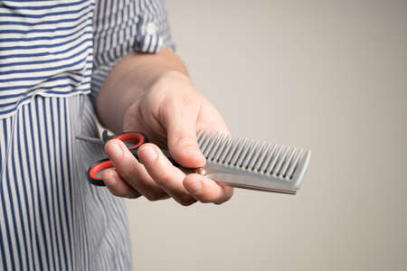 Preparing for hair cutting, scissors and comb in the hands of a woman on a beige background.の写真素材