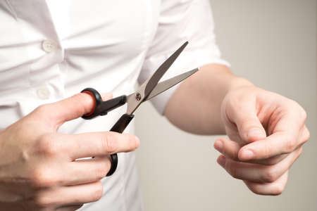 A woman in a white shirt is going to cut hair, scissors in her hands on a beige background.の写真素材