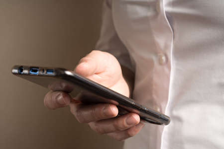 A woman in a white shirt holds a phone on a beige background. The concept of technology in business.