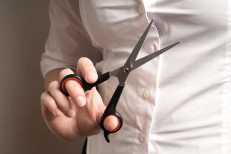 Scissors in the hand of a woman in a white shirt on a light background.の写真素材