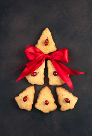 The cookies are laid out in the shape of a Christmas tree with a red bow on a brown concrete...
