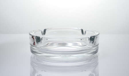 Transparent glass ashtray on a glossy light background. Side view.の写真素材