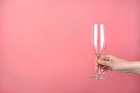 Hand holding an empty champagne glass on a pink background. Side view with space for copying. Concept of holiday backgrounds.の写真素材