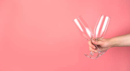 A woman holds two champagne glasses in her hand on a soft pink background. Panorama with space to copy. Concept of holiday backgrounds.の写真素材
