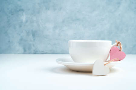 Two hearts are tied to the handle of a coffee Cup on a blue and white background. Side view with space for copying. Concept of holiday backgrounds.の写真素材