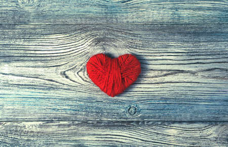 One red heart made of thread on a wooden textured gray-blue background. Top view with space to copy....