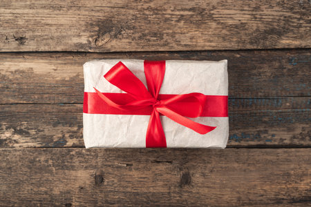Gift box tied with a red ribbon on a wooden background. Top view, with space to copy. The concept of holiday backgrounds.の写真素材