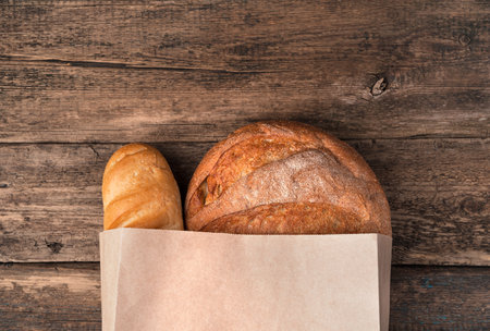 Fresh bread in a paper bag on a wooden background. Top view, with space to copy. The concept of natural products.の写真素材