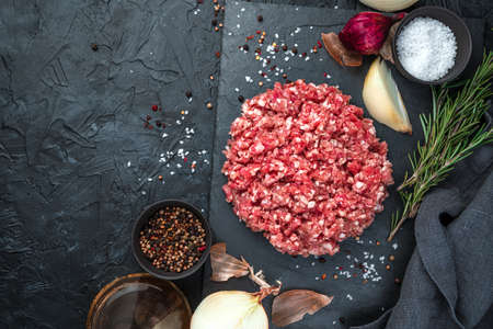 Fresh minced meat with onion and rosemary on a black background. Top view, with space to copy. The...