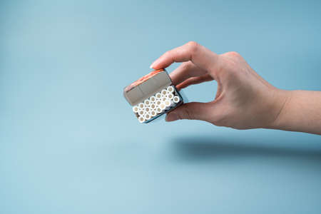 An open pack of cigarettes in a womans hand on a light blue background. Side view with copy space....
