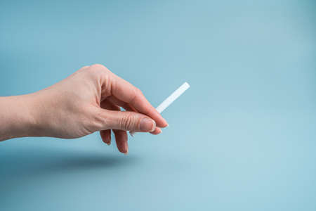 A cigarette in the hand of a woman on a blue background. Side view, horizontal, with space to copy.