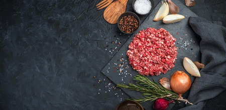 Ground turkey meat with pepper, onion and rosemary on a black concrete background. Side view,...