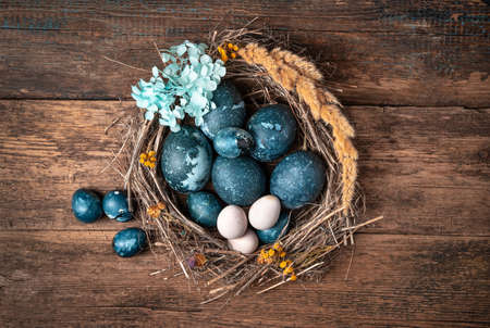 The nest is decorated with blue flowers with Easter marble-blue eggs on a wooden background. Chicken and quail eggs in a beautiful nest.の写真素材