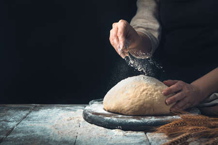 The dough is sprinkled by the cooks hand on a dark background. Vintage background with copy space.の写真素材