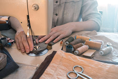 A woman tailor sews on a sewing machine. Side view. The concept of sewing.