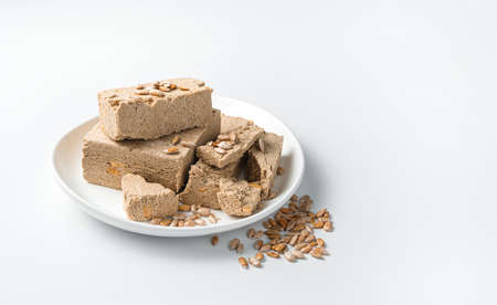A white plate with halva is sprinkled with sunflower seeds on a light background. Minimalistic...