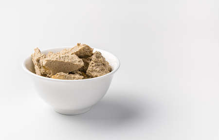 Small pieces of halva in a cup on a light background. Side view with copy space. The concept of...