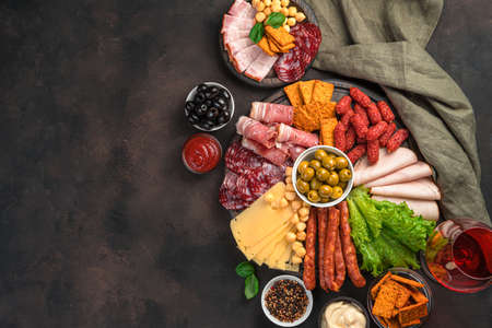 Charcuterie board. Different types of sausages, cheese, lettuce and olives on a brown background....
