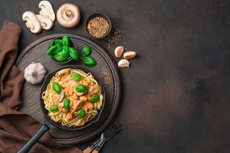 Culinary background with pasta and creamy mushroom sauce, basil, garlic and spices on a dark brown background. Top view, with space to copyの写真素材