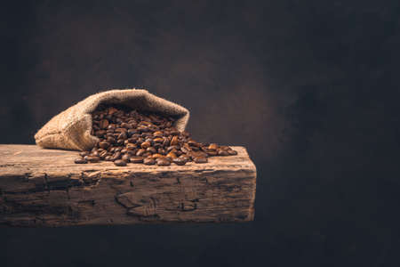 Coffee beans in a linen bag on a wooden board on a brown background. Side view, copy space.