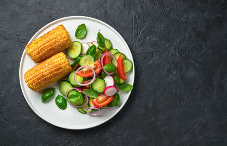 Salad with fresh, juicy vegetables and roasted corn on a black background with space to copy. Healthy, vegetarian food.の写真素材
