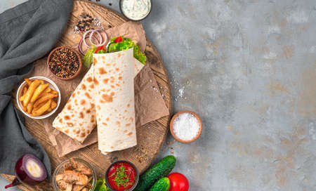Fast food: shawarma, burrito on a gray background with ingredients. Top view, copy space.
