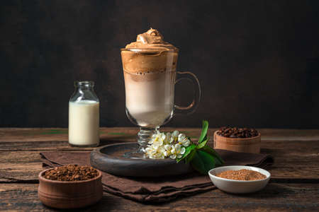 Korean dalgona coffee with foam and ice on a brown background. Side view, horizontal. An...