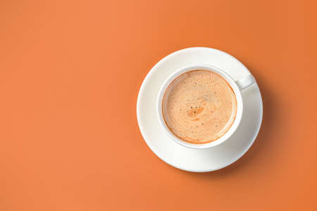 Coffee in a white cup and saucer on a terracotta background. Morning cappuccino. Top view, copy space.の写真素材