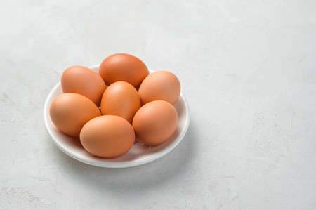 Chicken eggs on a white plate on a gray background. Side view, copy space.