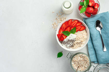 Healthy oatmeal porridge with strawberries, chia seeds and yogurt on a gray background with space to copy. Healthy diet food.の写真素材