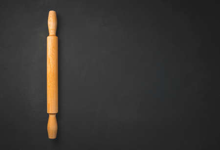Kitchen rolling pin on black background with copy space. Culinary background.