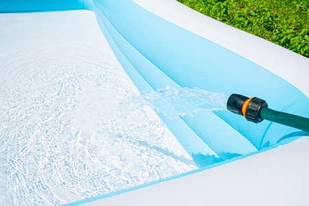 Filling the garden children's pool with water on the green lawn. Side view, horizontal.