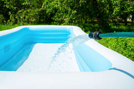 The inflatable garden pool is filled with water from a hose. Selective focus. Side view, space for copying.の写真素材