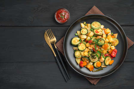 Baked vegetables, sauce and cutlery on a black background. Top view, copy space.の写真素材