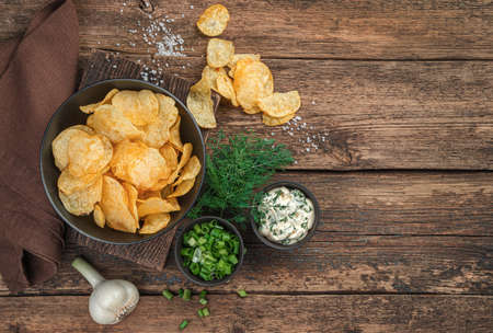 Potato chips, fresh herbs and sauce on a wooden background. Top view, copy space.の写真素材