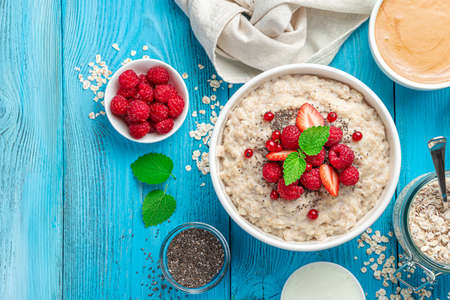 Oatmeal porridge with berries and chia seeds in a white bowl on a blue background. Top view, copy space.の写真素材