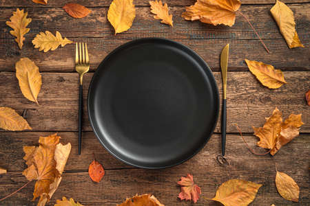 A black plate and cutlery among autumn leaves on a wooden background. Top view.の写真素材