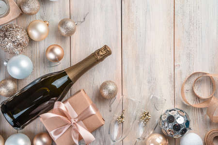 Christmas background with champagne, gift box and Christmas tree toys on beige background. Top view, copy space.