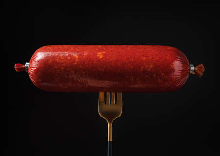 Smoked sausage on a fork on a black background. Side view, close-up.の写真素材