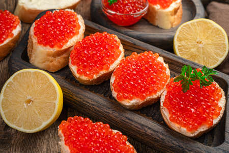 Sandwiches with red caviar, butter, parsley and lemon on a wooden background. Side view, close-up.の写真素材