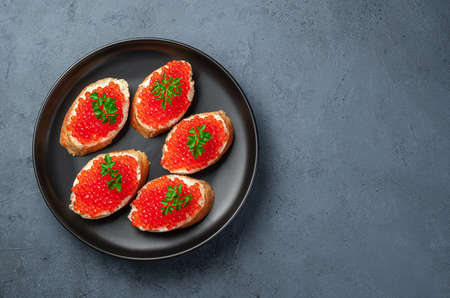 Sandwiches with red caviar in a black plate on a dark blue background. Seafood appetizer.の写真素材