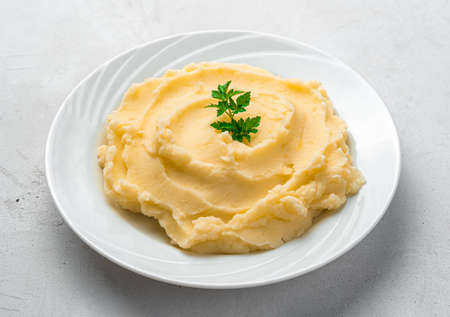 Mashed potatoes with basil in a white plate close-up on a gray background. Side view, horizontal.の写真素材
